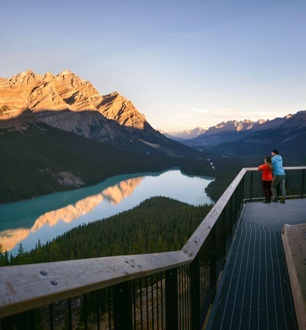 A couple stand on the viewing deck looking out at the view of Peyto Lake and the surrounding mountains.